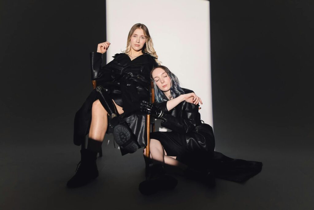 Two fashion models posing in stylish black attire under a dramatic spotlight.